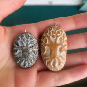 2 pendentifs sculptés à partir de petits galets représentant chacun un arbre.